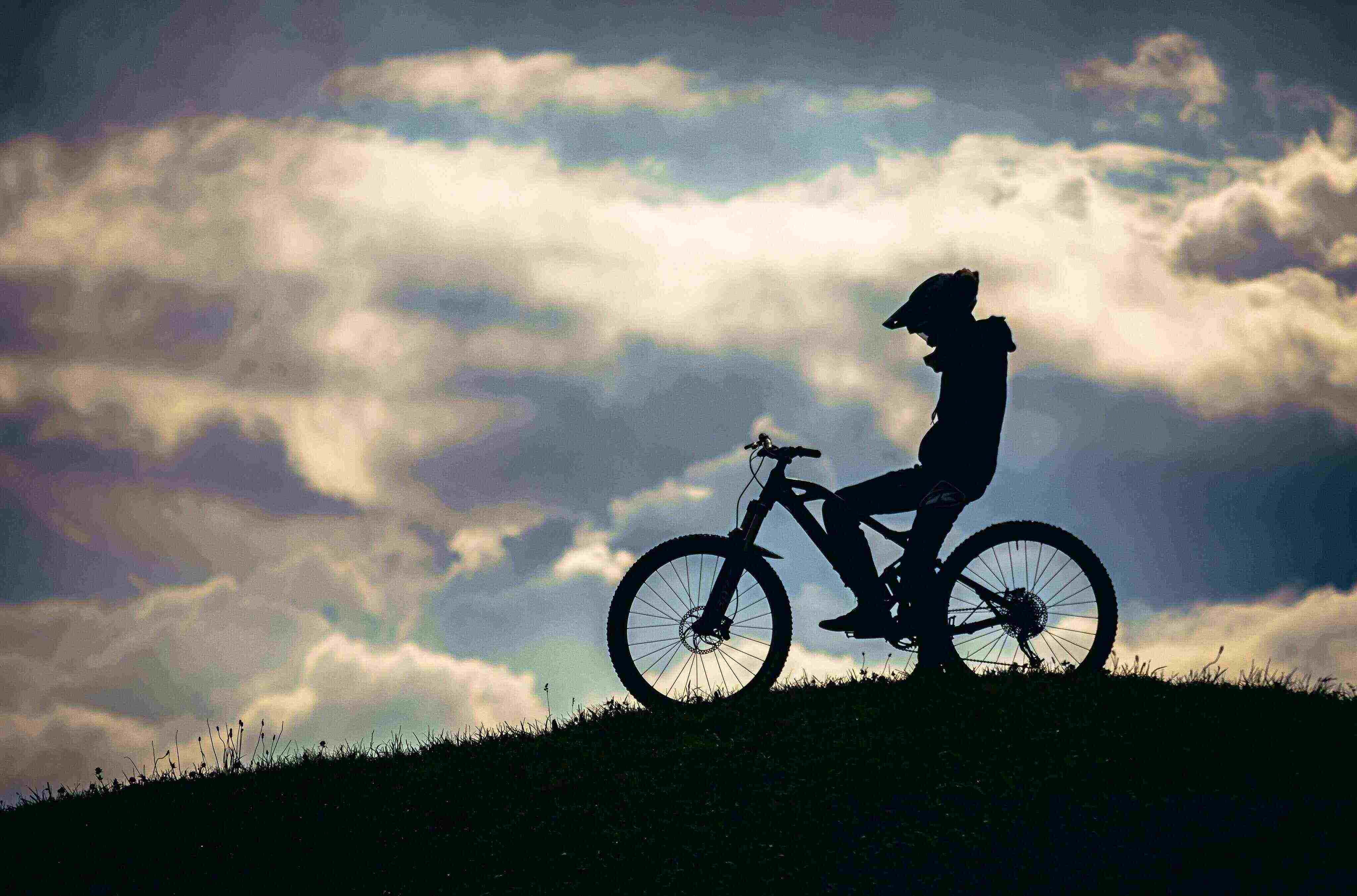 Silhouette of biker on hill against cloudy backdrop